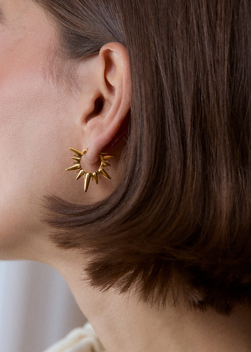 Close-up of an 18k gold vermeil sunburst hoop earring worn on the ear.
