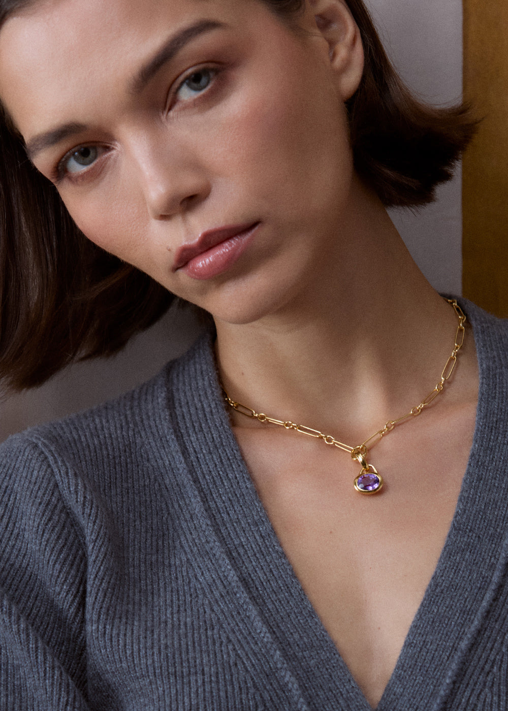 Purple amethyst pendant on an 18k gold vermeil link necklace, worn with a grey cardigan.