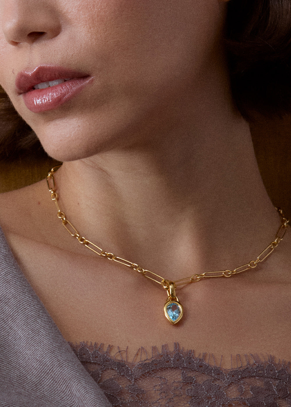 Close-up of a pear-shaped blue topaz pendant worn on an 18k gold vermeil rectangular-link chain.