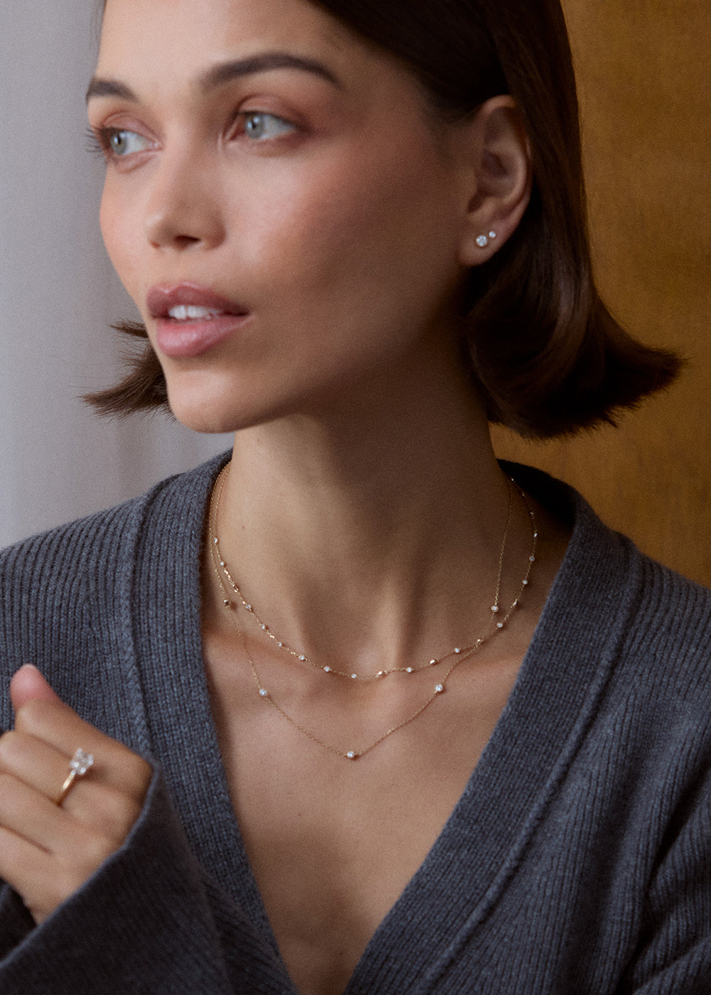 Layered fine necklaces with spaced diamonds and small pendants, worn at the neckline.
